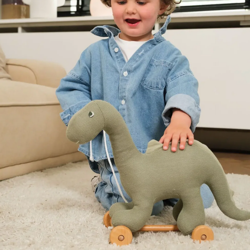 Child playing with a green dinosaur toy on a carpeted floor.