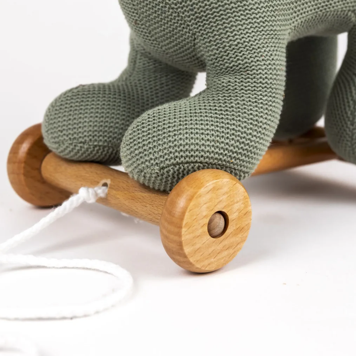 Green knitted baby booties with wooden wheels on a white background