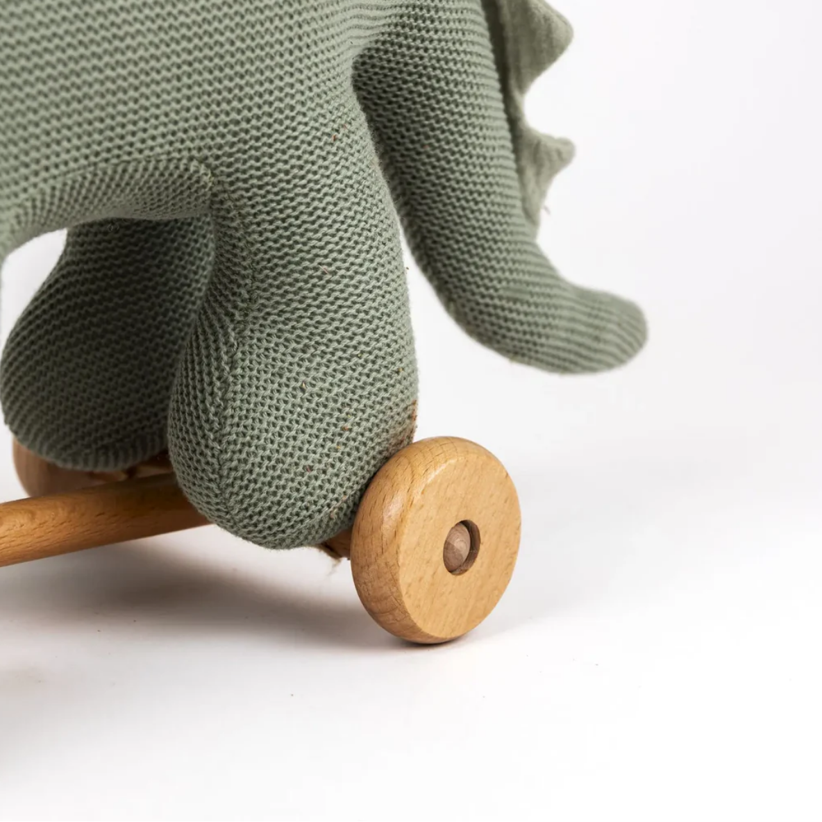 Green knitted toy elephant with wooden wheels on a white background