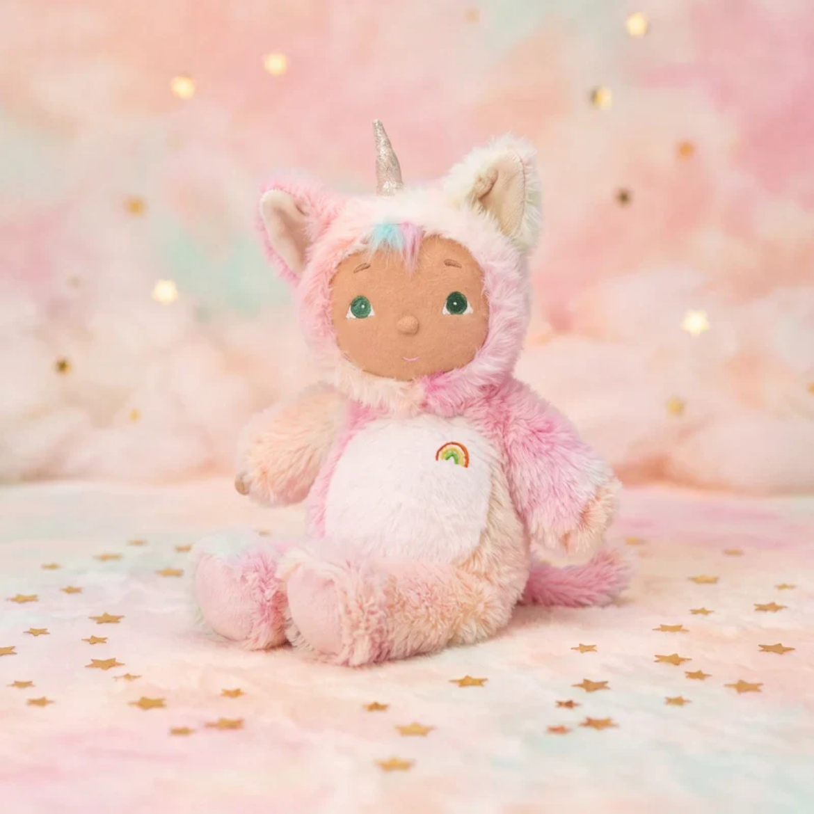 Stuffed toy in a pink unicorn costume on a soft, pastel background with gold stars.