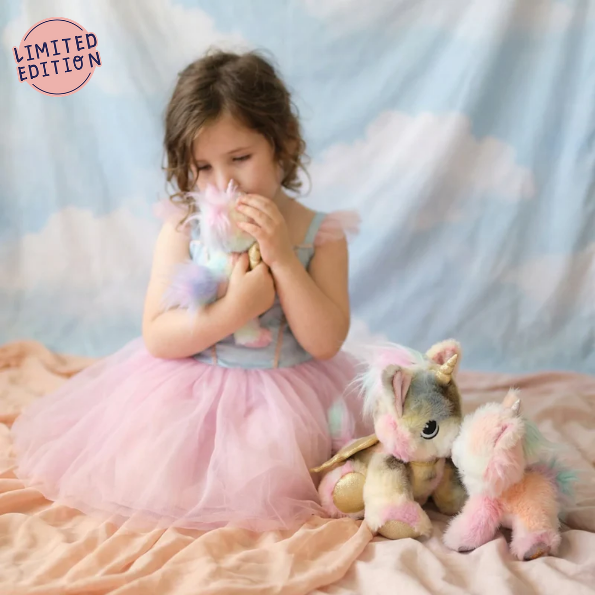 Young girl in a pink dress with a unicorn toy on a cloud-themed background