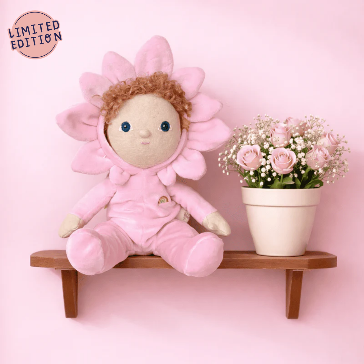 Pink plush toy with flower design sitting on a wooden shelf against a pink background