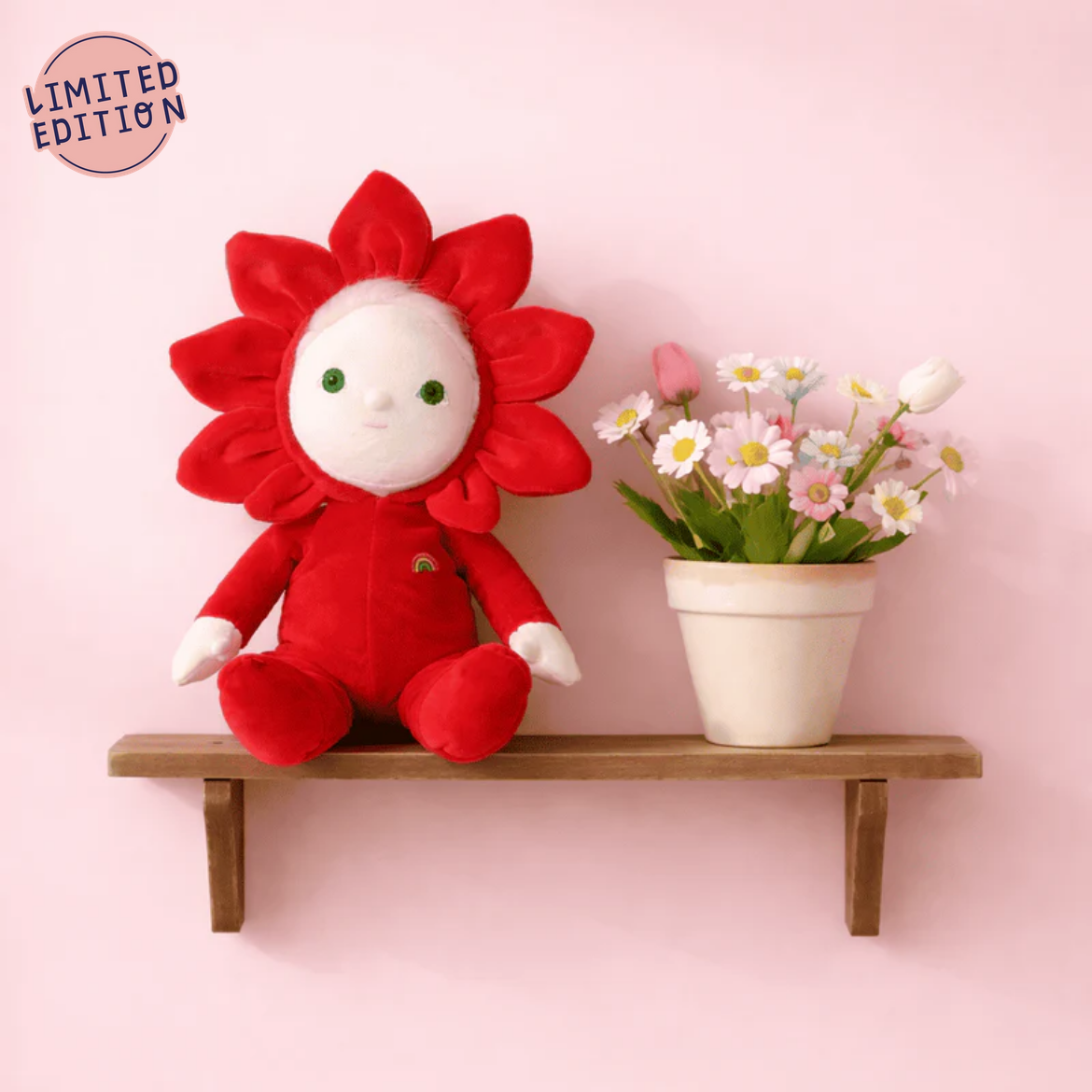 Red plush flower toy on a wooden shelf with a pink background