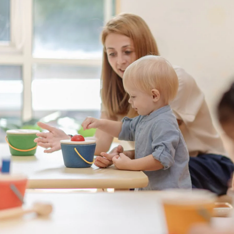 Woman and child at a table with colorful bowls and utensils in a bright room.