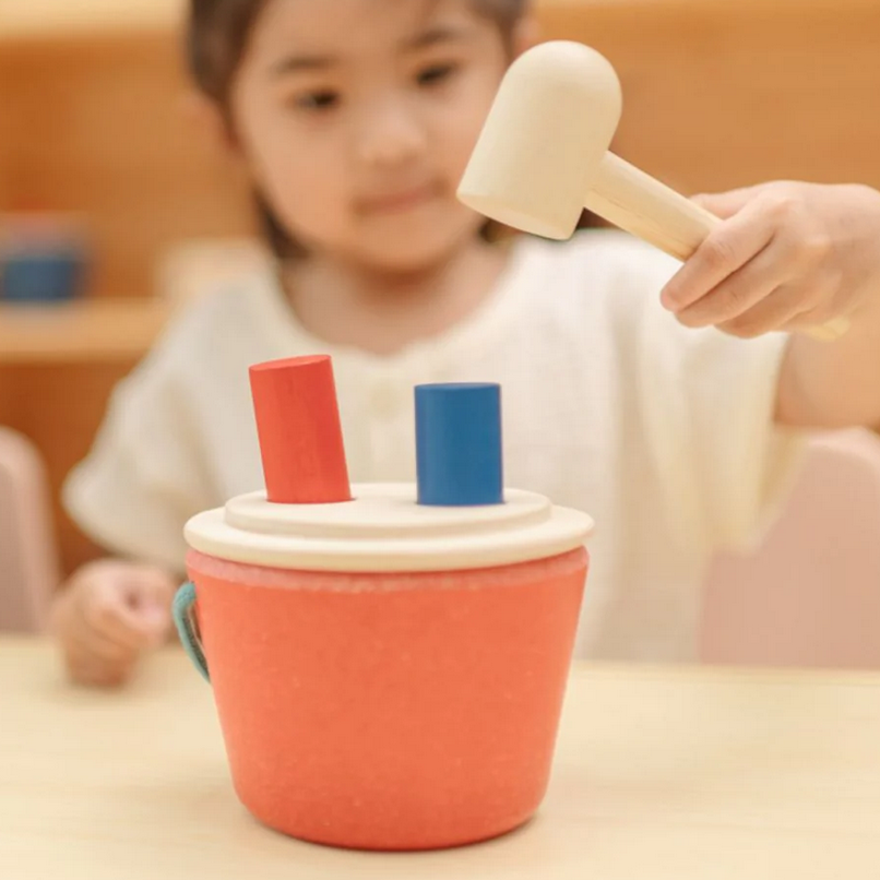 Child playing with a wooden toy hammer and cups on a table.