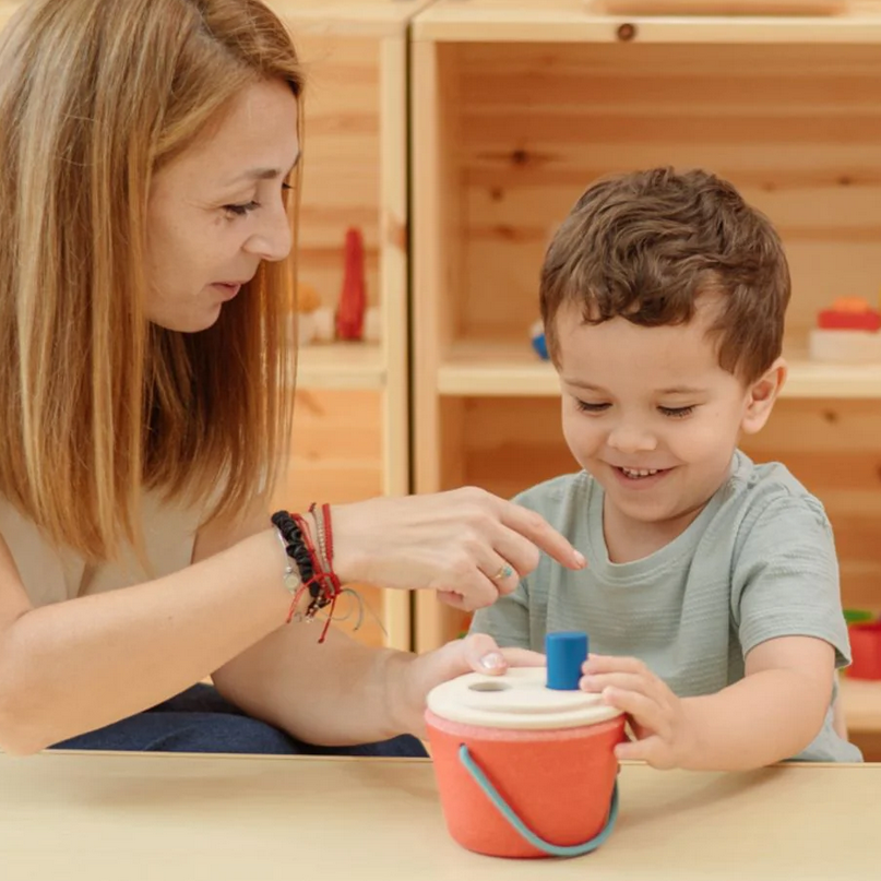 Woman and child playing with a colorful toy in a wooden classroom setting