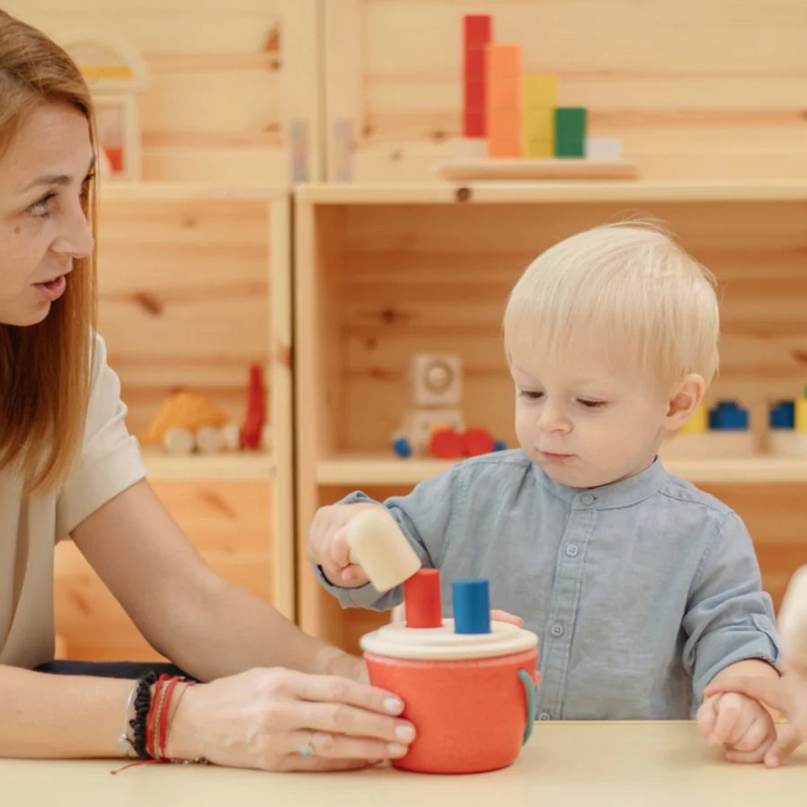 Woman and child playing with a colorful toy in a wooden playroom