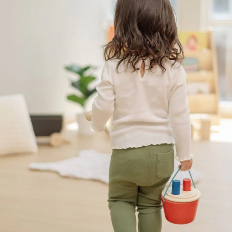 Child walking with a colorful bucket in a room with a blurred background