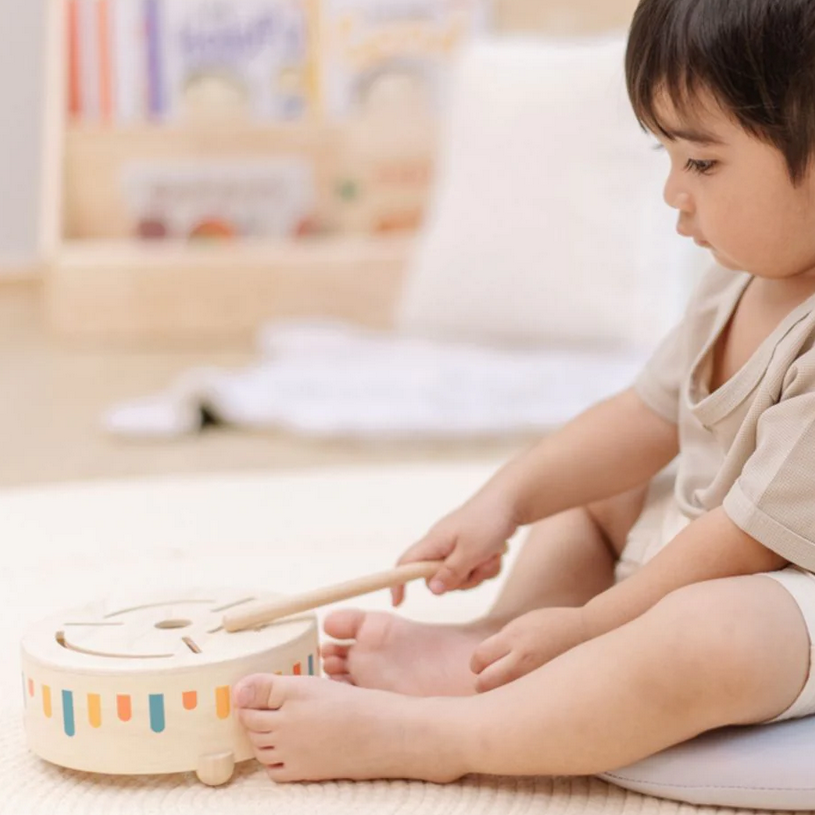 Child playing with a colorful toy drum in a bright room