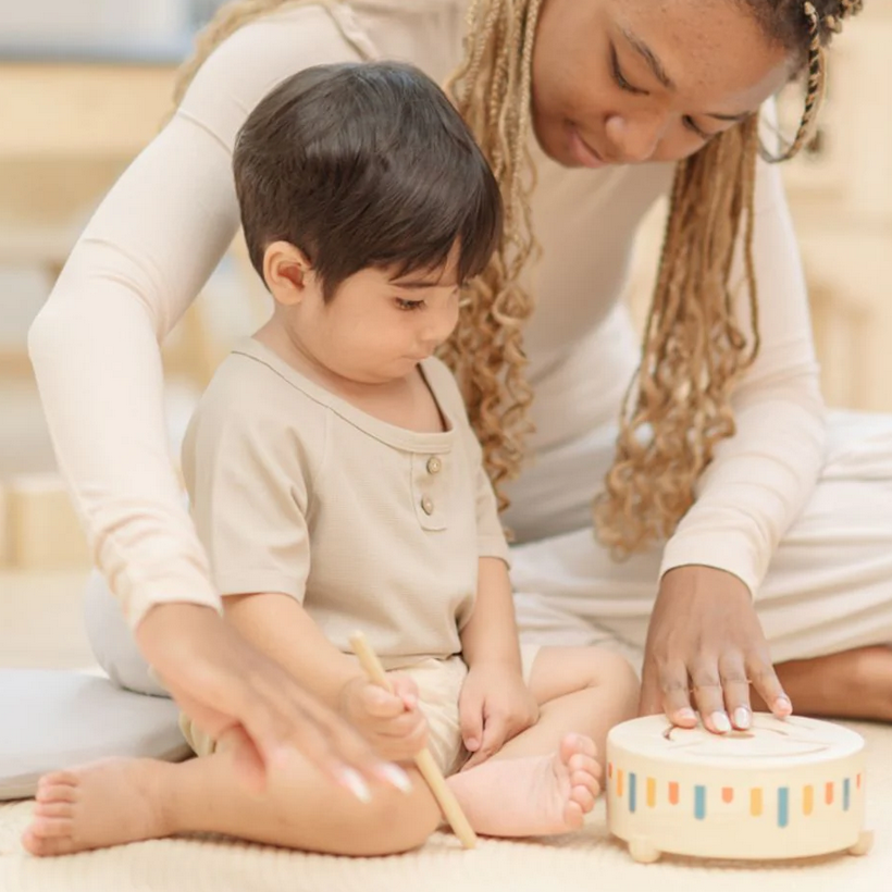 Woman and child playing with a wooden toy on a light-colored floor.
