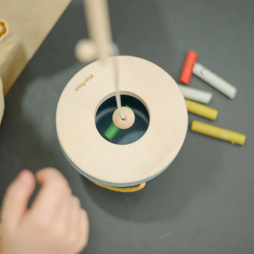 Wooden toy with colorful sticks on a dark surface, child's hand reaching towards it.