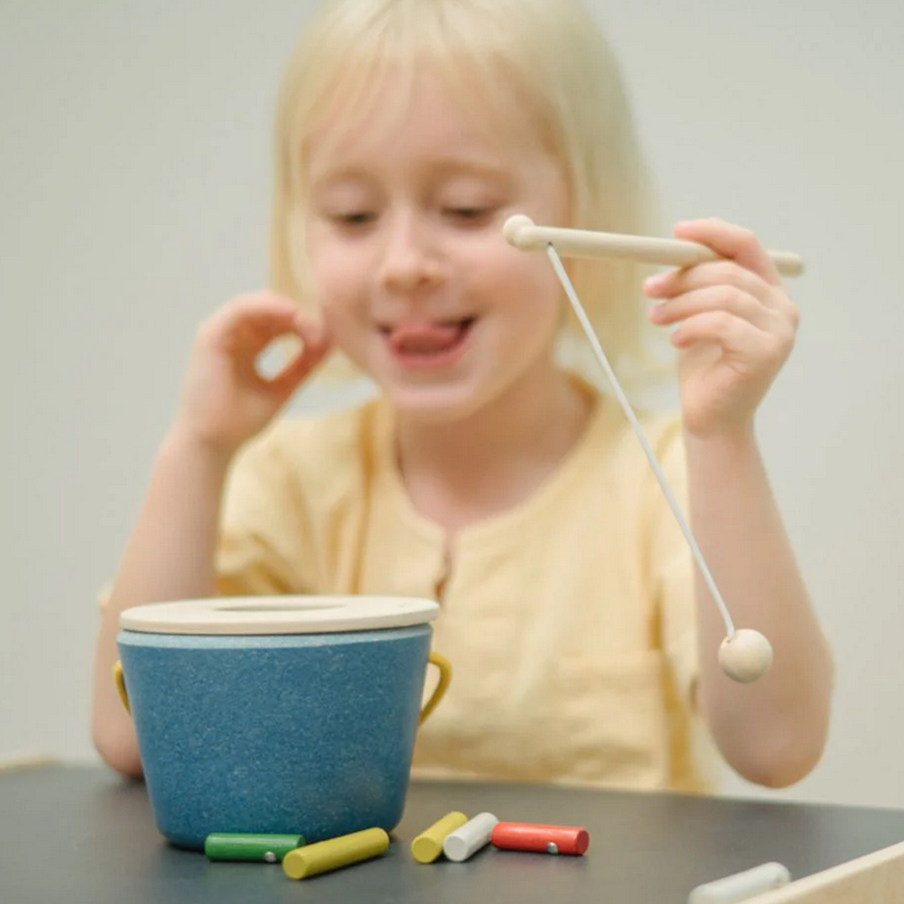 Child playing with a blue bowl and colorful sticks on a table.