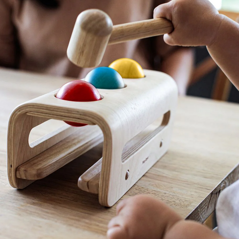 Child playing with a wooden toy hammer and colorful balls on a table.