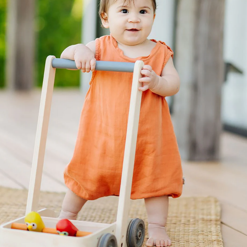 Child in an orange dress standing with a toy cart outdoors