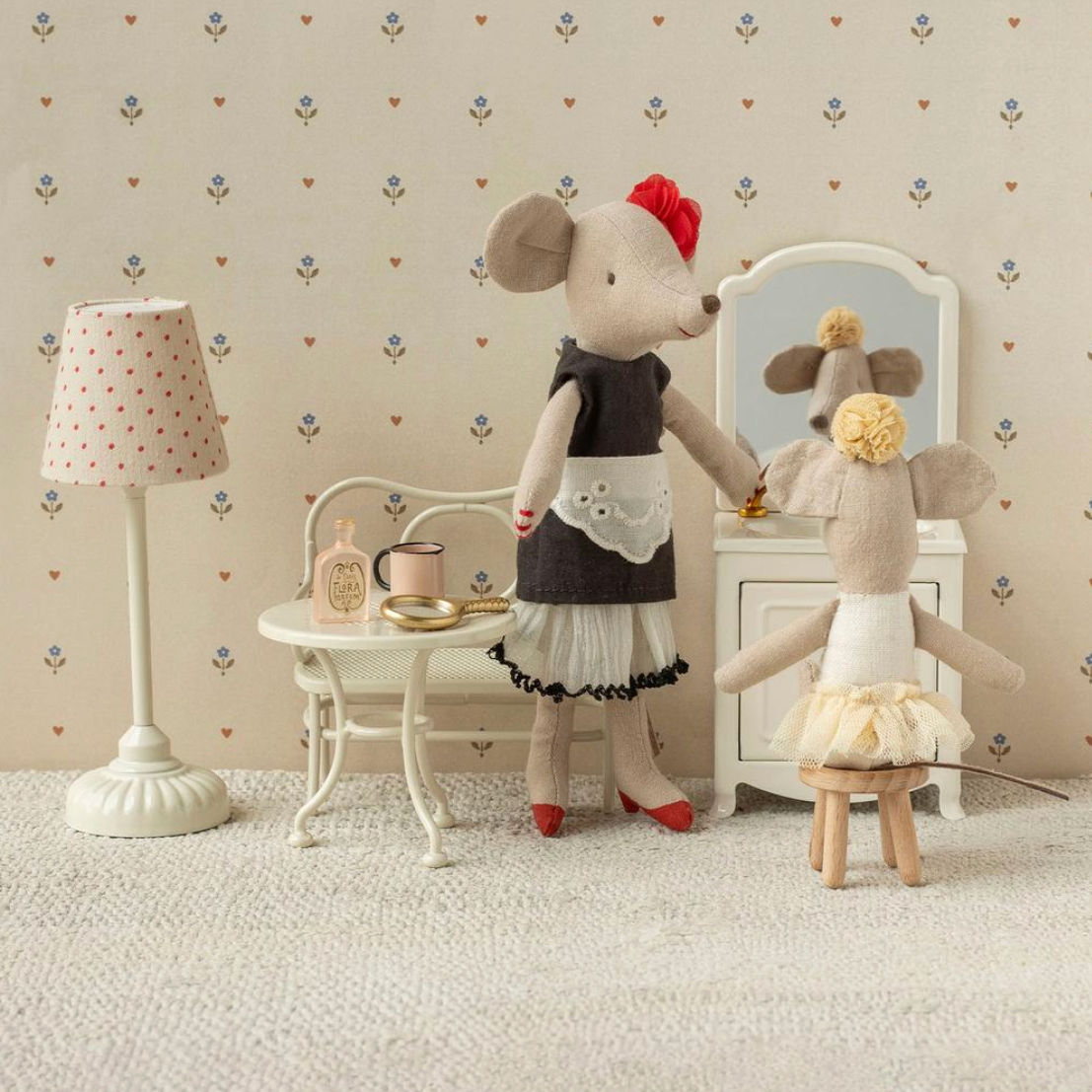 Two toy mice in a room with a lamp and vanity mirror.