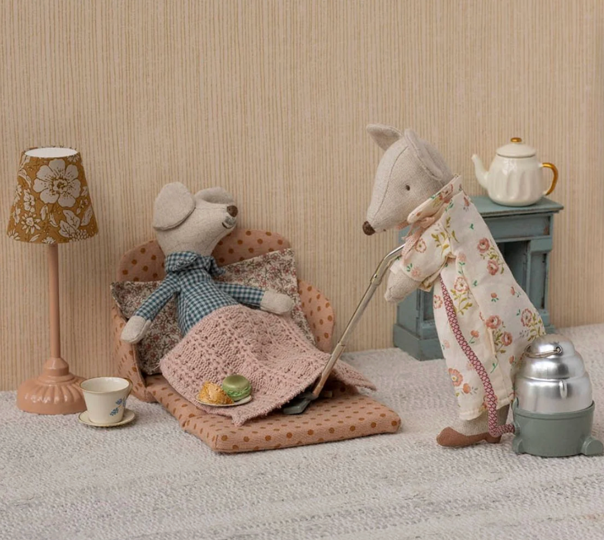 Two stuffed animals in a room setting with a lamp, table, and teapot.