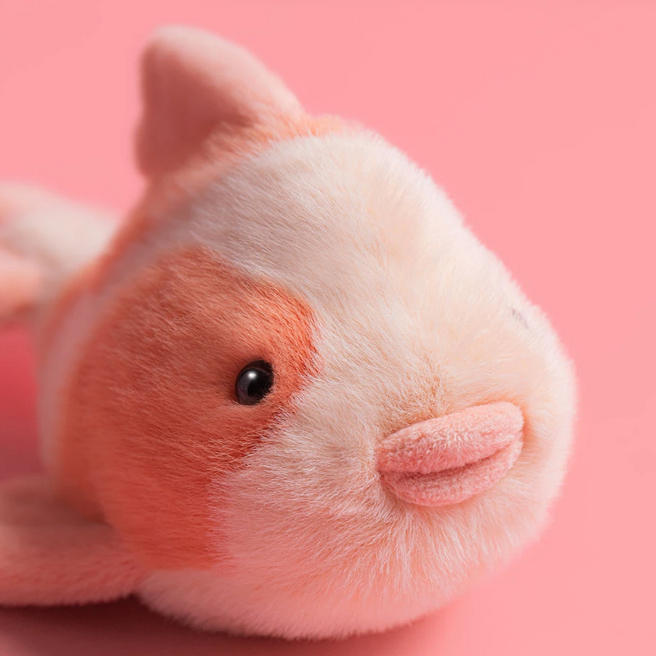 Plush toy resembling a fish with pink and orange colors on a pink background