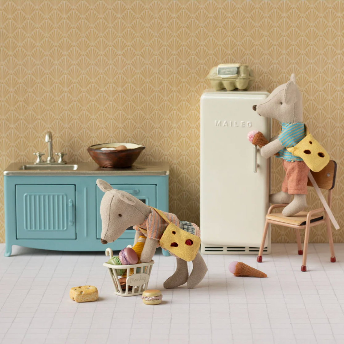 Two toy mice in a kitchen setting with a refrigerator and sink.