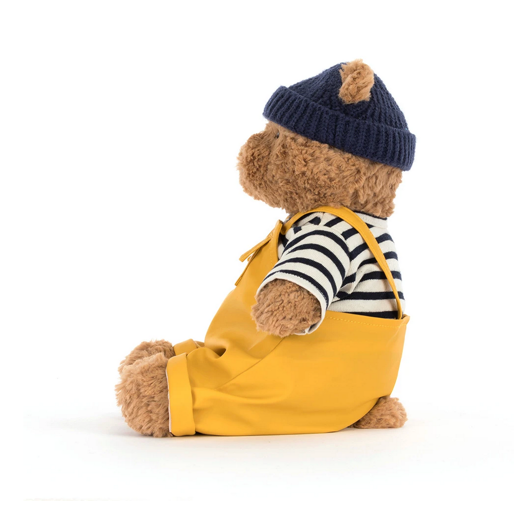 Teddy bear wearing a yellow outfit with a striped shirt and navy hat on a white background