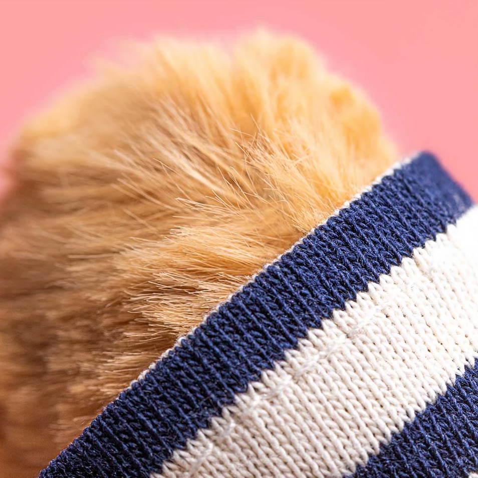 Close-up of a bear wearing a blue and white striped outfit with a pink background.