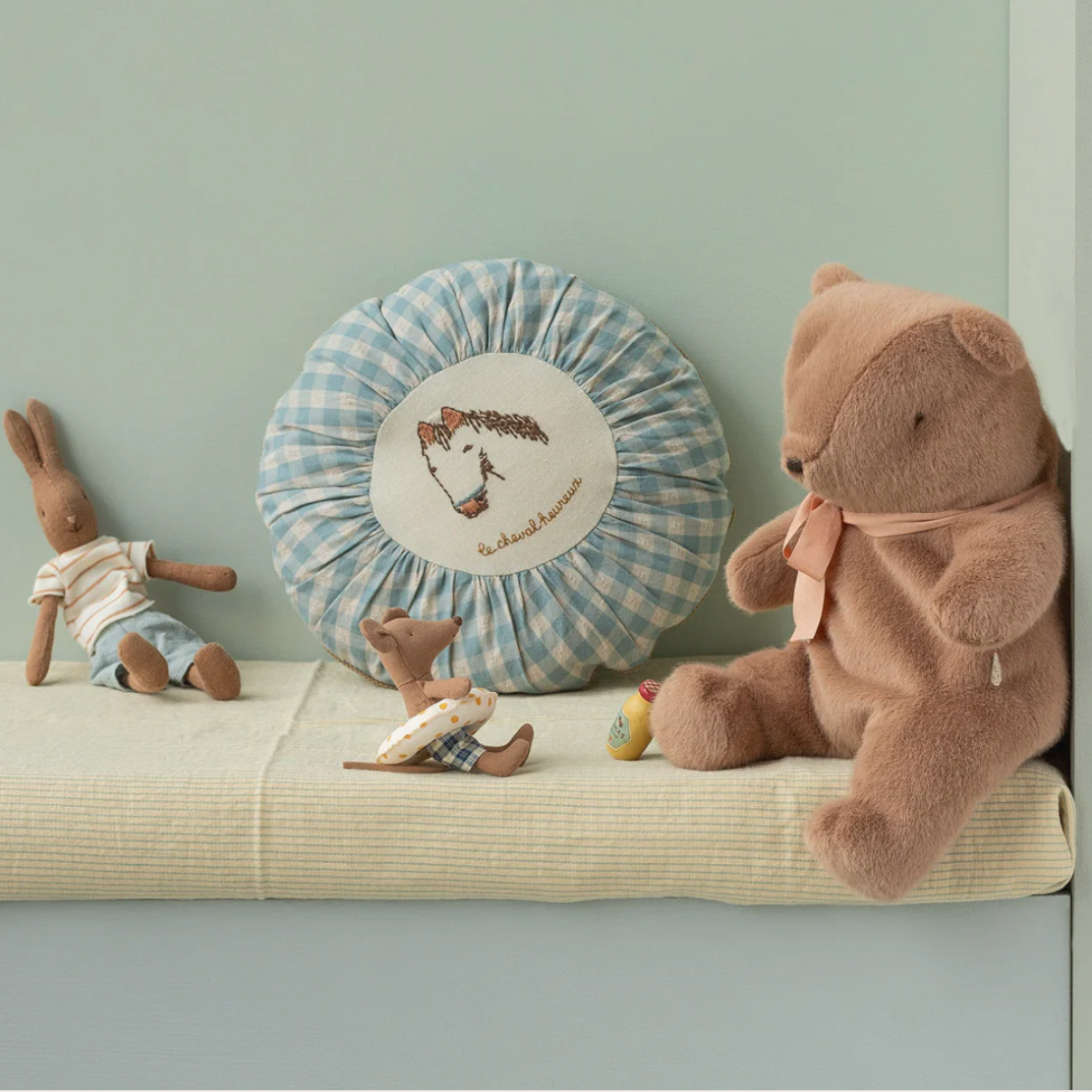 Children's toys including a teddy bear and rabbit on a cushion against a light green wall.