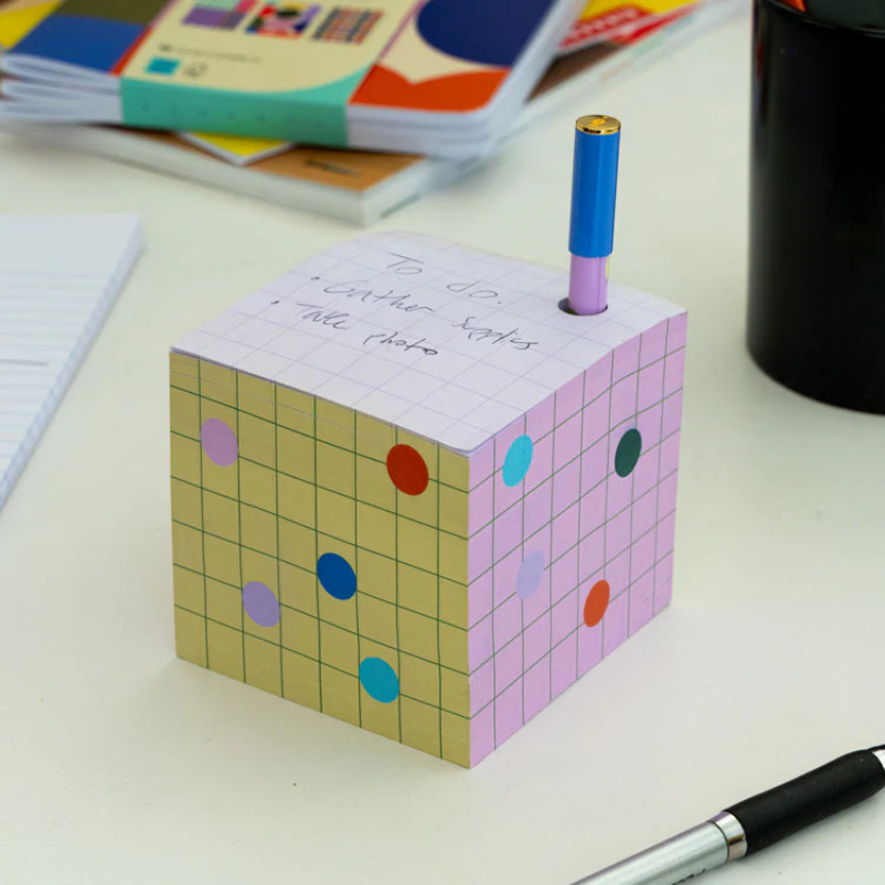 Colorful cube-shaped sticky note holder with a pen on a desk