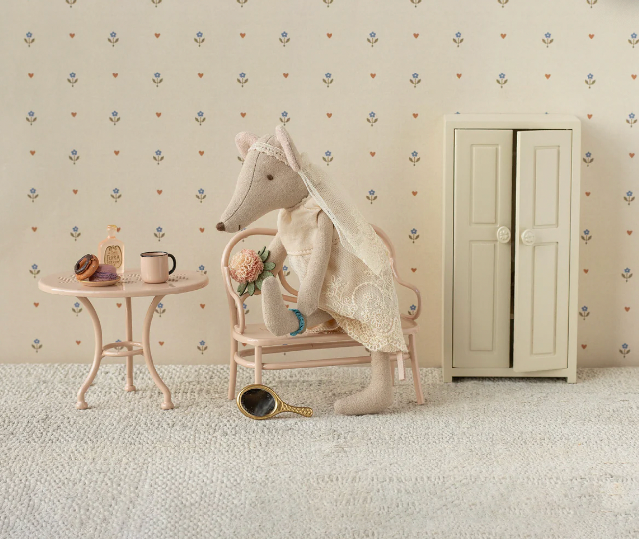 Decorative scene with a stuffed animal, table, and cabinet against a patterned wall.