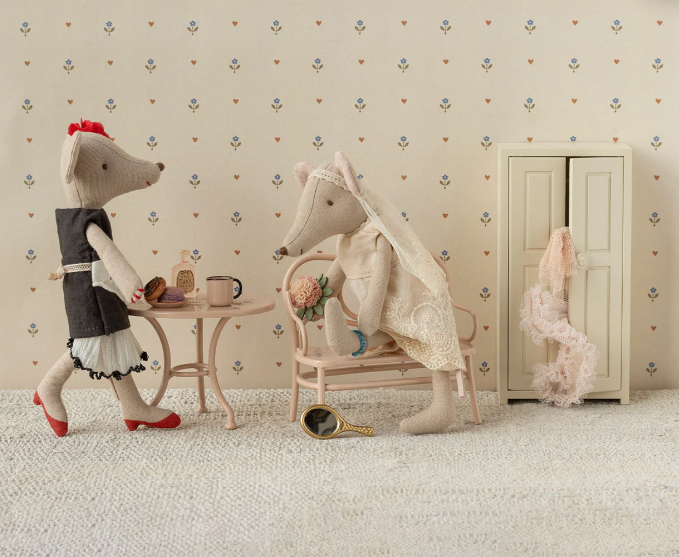 Two plush toys, a rabbit and a dog, in a room with a floral wallpaper and a small table.