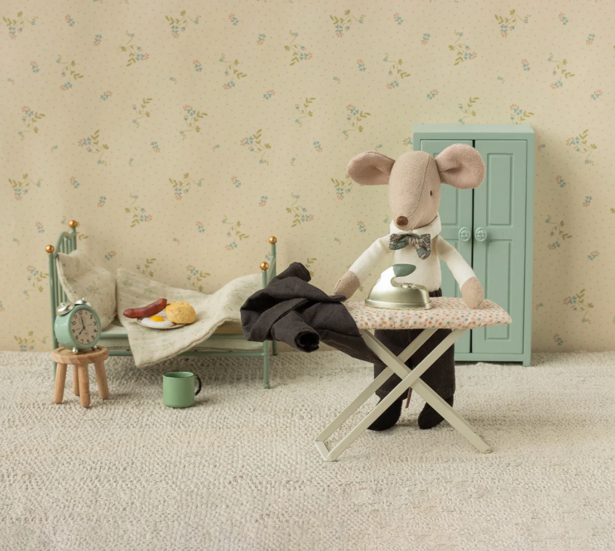 Toy mouse on an ironing board with a child's bed and dresser in the background