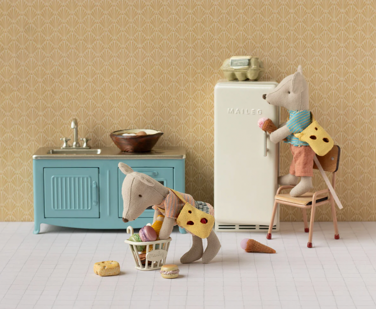 Children's play kitchen set with toy animals and furniture against a patterned wall.