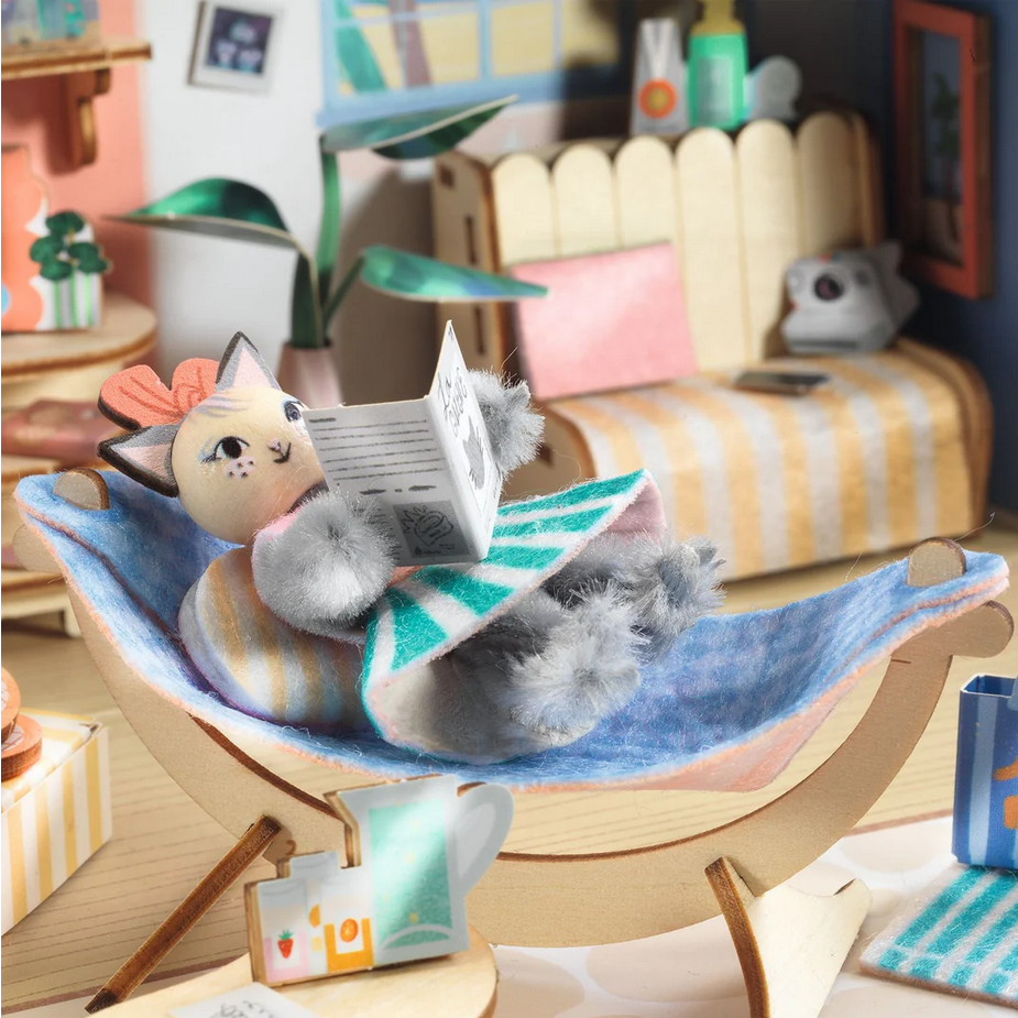 Cat-shaped toy reading a book on a hammock in a cozy room setting