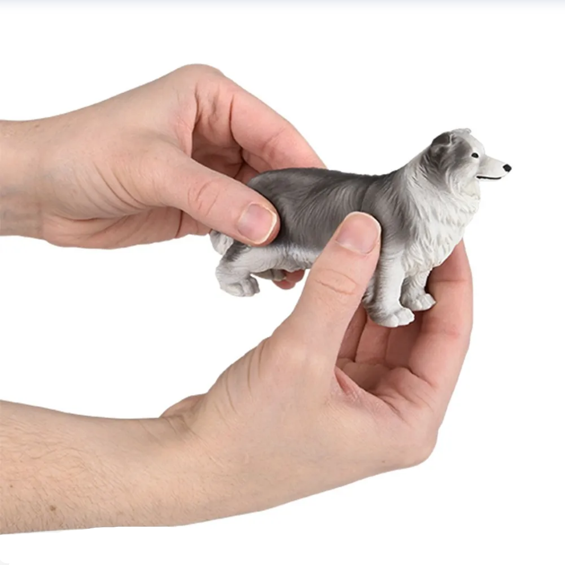 Hand holding a small dog figurine against a white background