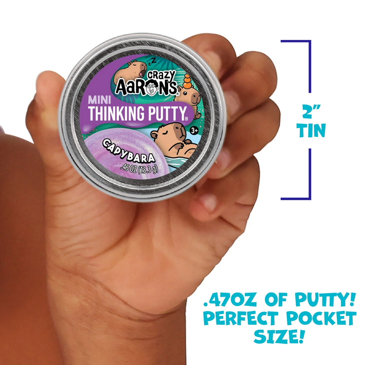 Hand holding a small container of Crazy Aaron's Thinking Putty with product details on a white background