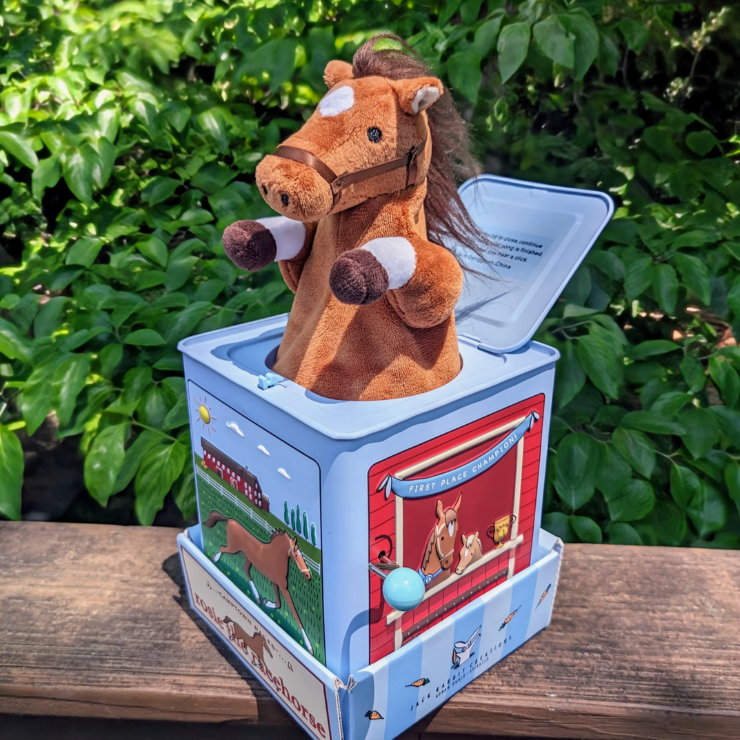Plush horse toy in a blue box with a wooden surface and green foliage background