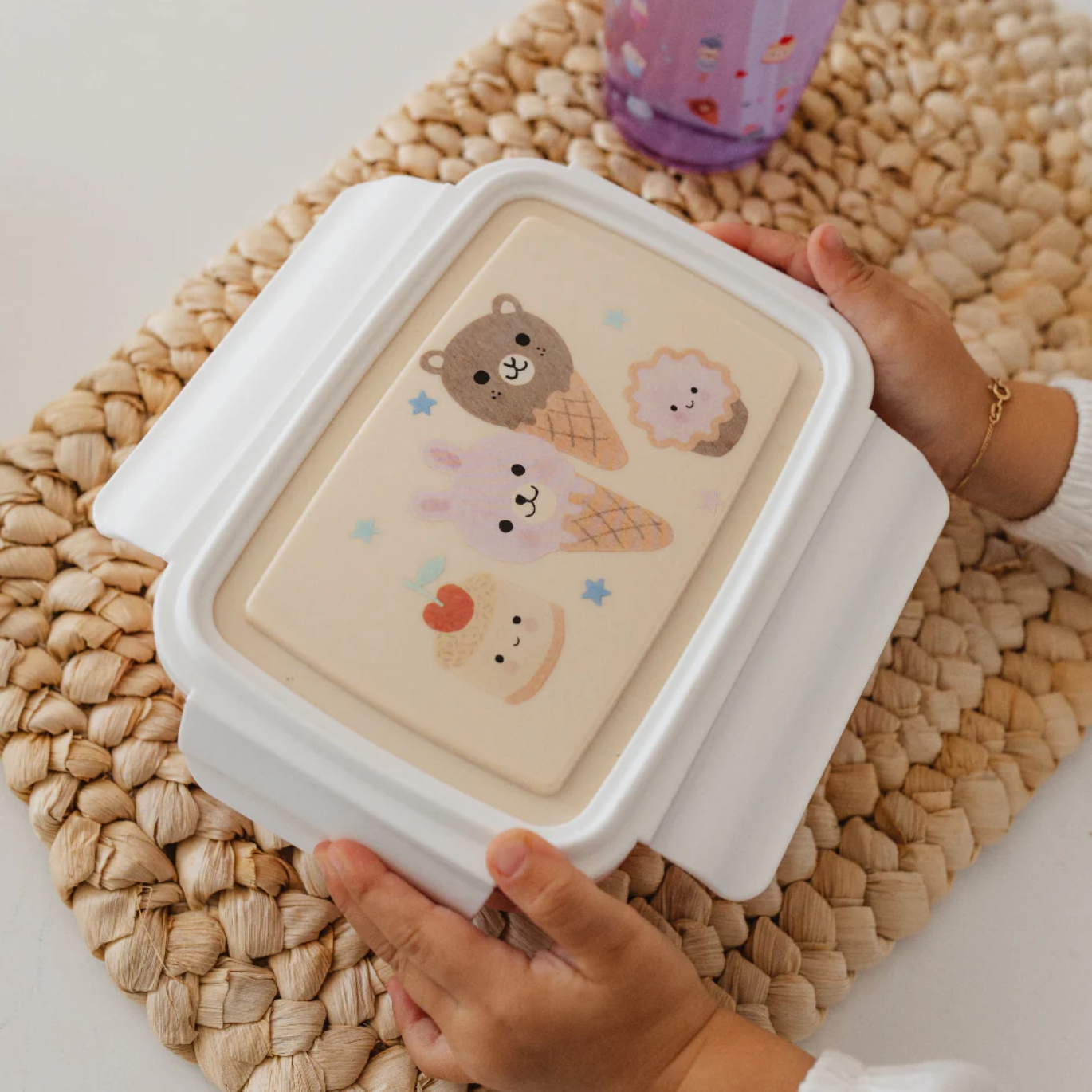Bento box with bear and ice cream illustrations held by a person on a woven mat.
