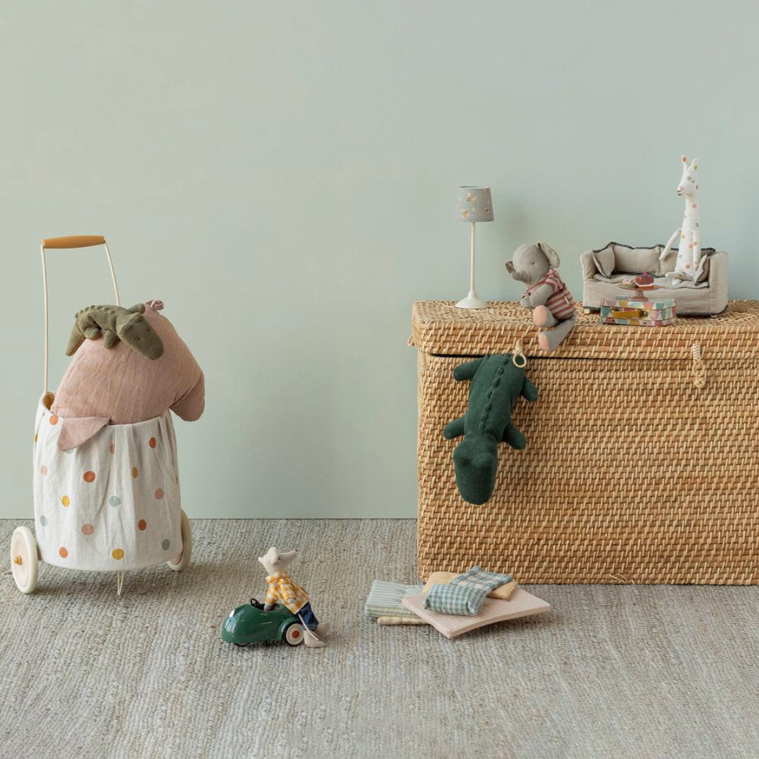 Children's toys including a toy pig, toy crocodile, and a wicker storage basket on a light gray floor.