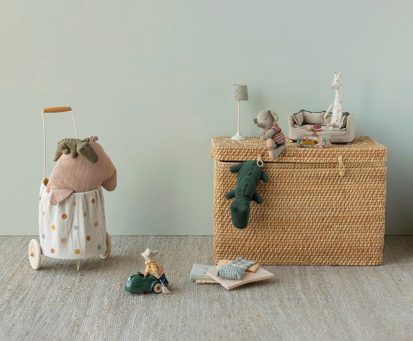 Children's toys including a toy car, dolls, and a woven storage basket on a light gray floor.