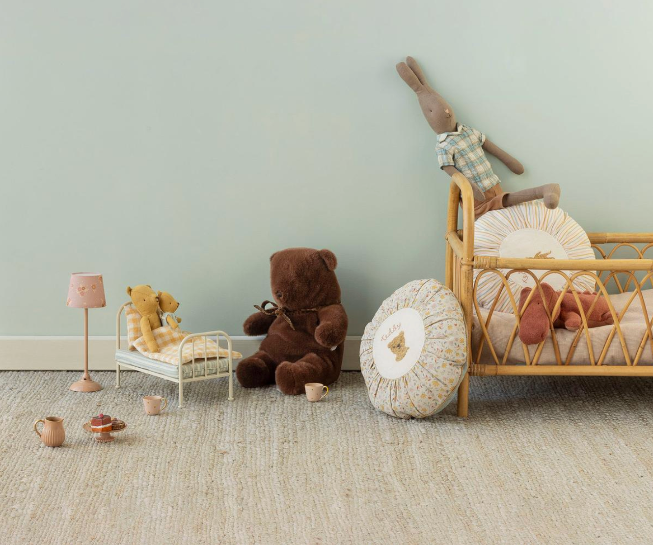 Children's room with a small bed, teddy bear, and decorative items against a light green wall.
