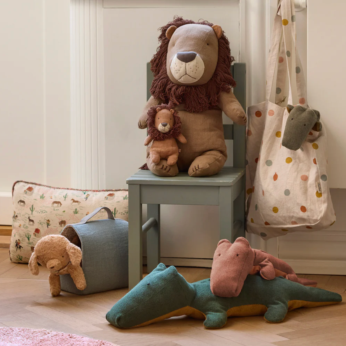 Plush toys including a lion, teddy bear, and alligator on a chair and floor in a room.
