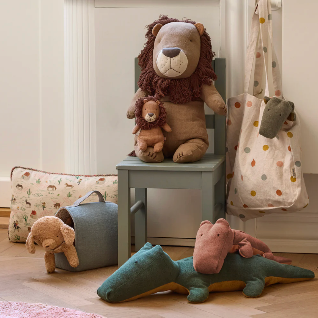 Plush toys including a lion, teddy bear, and alligator on a chair and floor in a room.