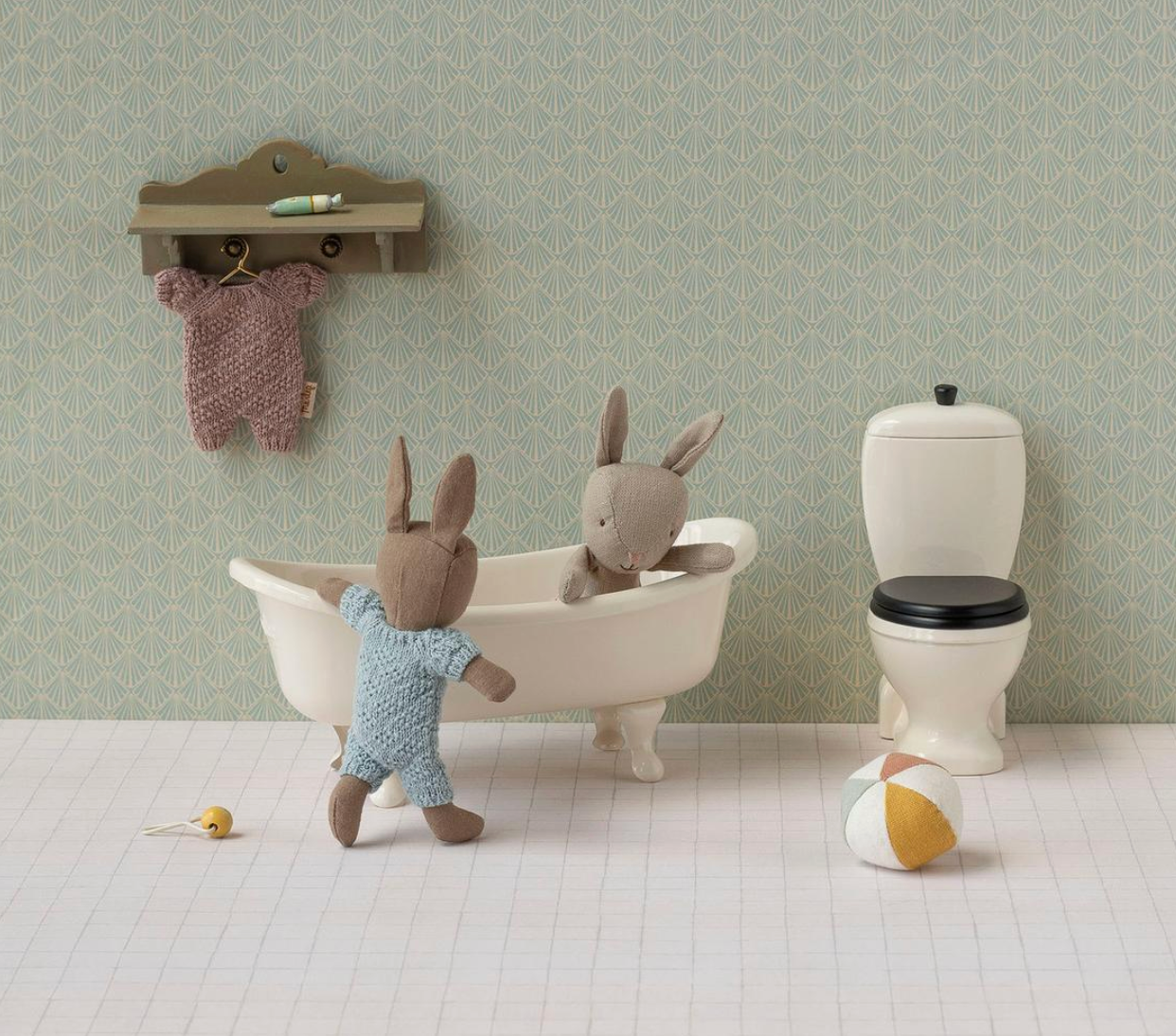 Two stuffed rabbit toys in a bathtub with a toilet and shelf in a bathroom setting.