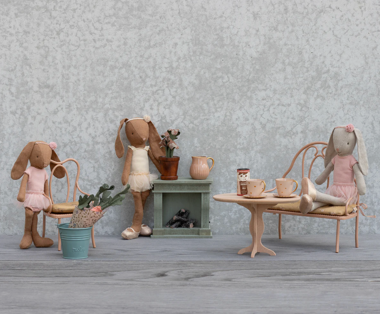 Miniature dollhouse scene with rabbits and furniture against a textured wall.
