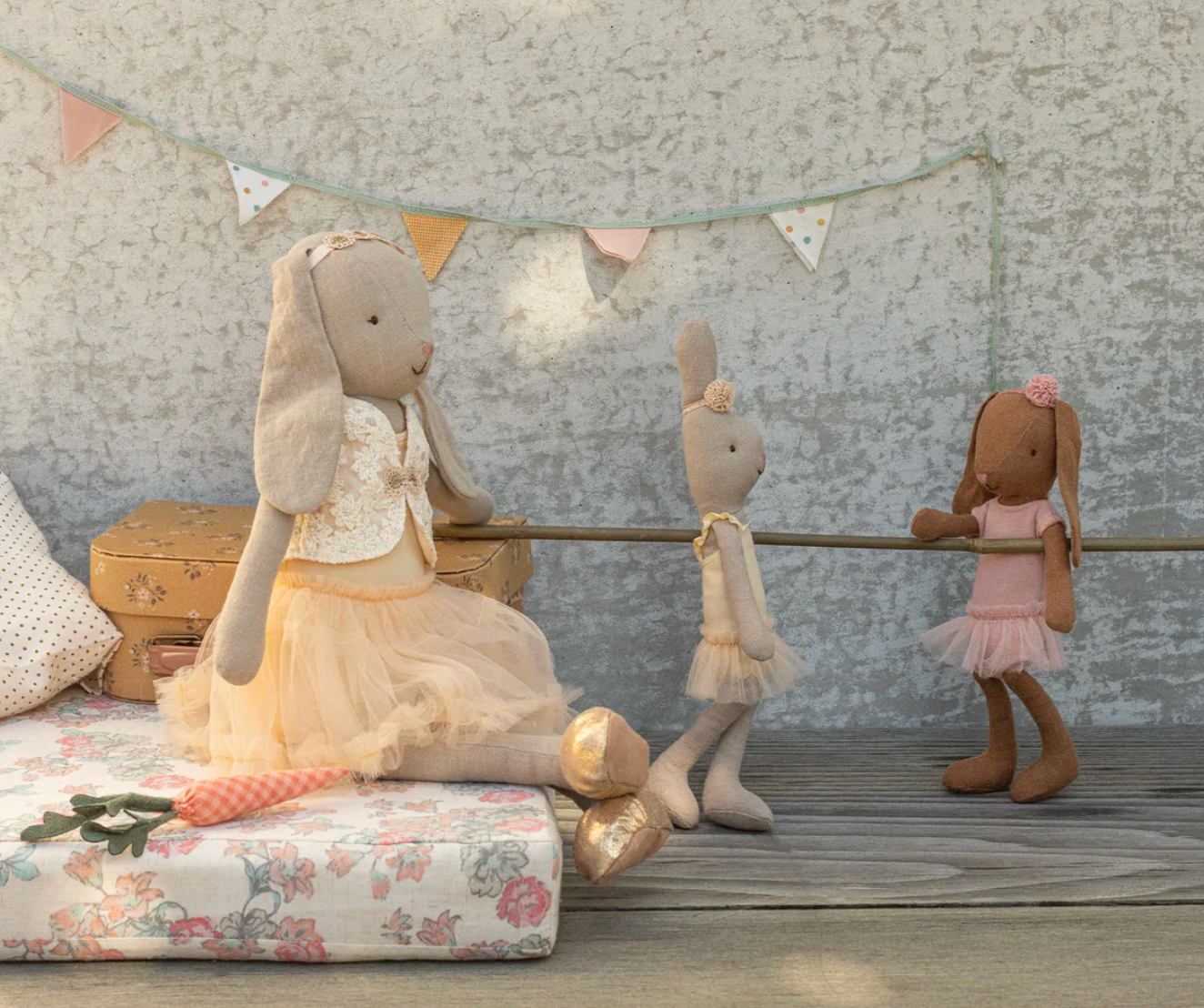 Three plush toys, including a rabbit and two other characters, on a wooden floor with a decorative banner in the background.