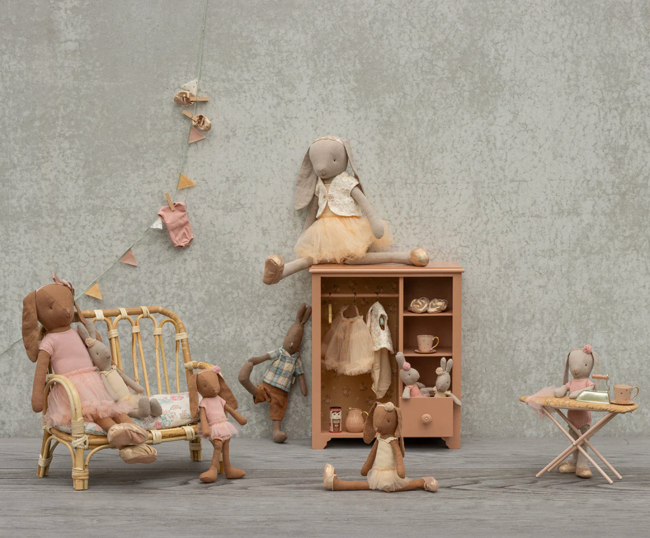 Toy room setup with dolls and furniture against a gray wall.