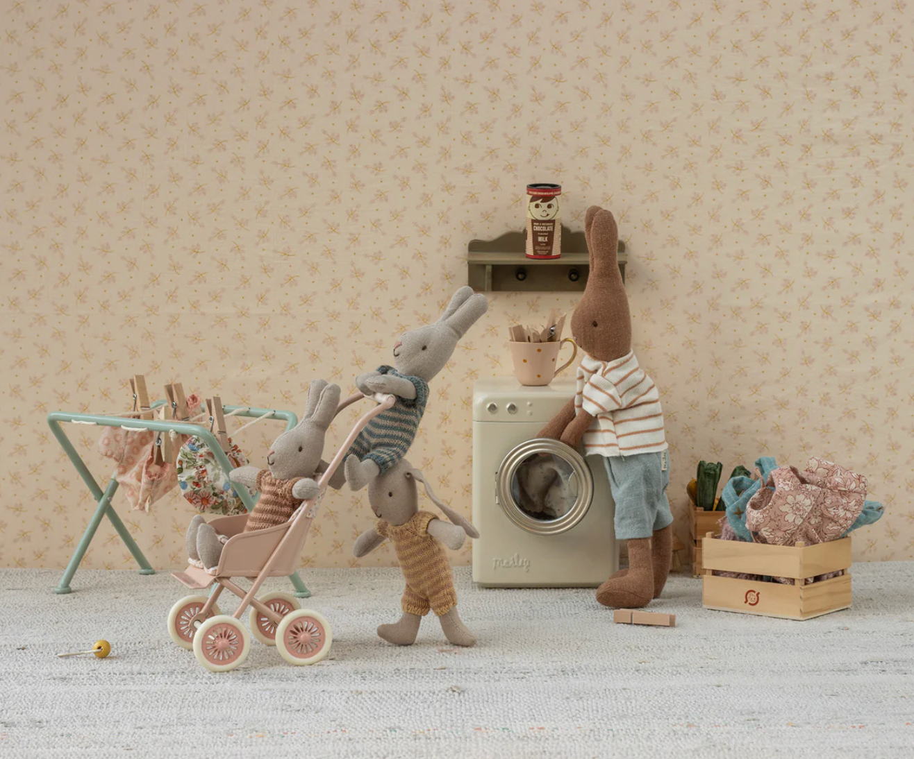 Toy scene with plush animals around a washing machine in a room with patterned wallpaper.