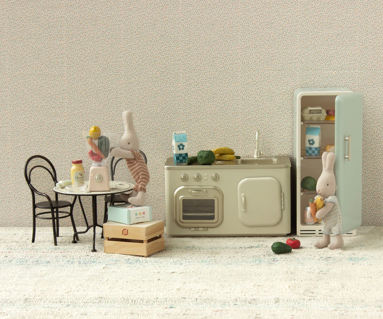 Miniature kitchen set with refrigerator, oven, and table with toys on a textured wall background