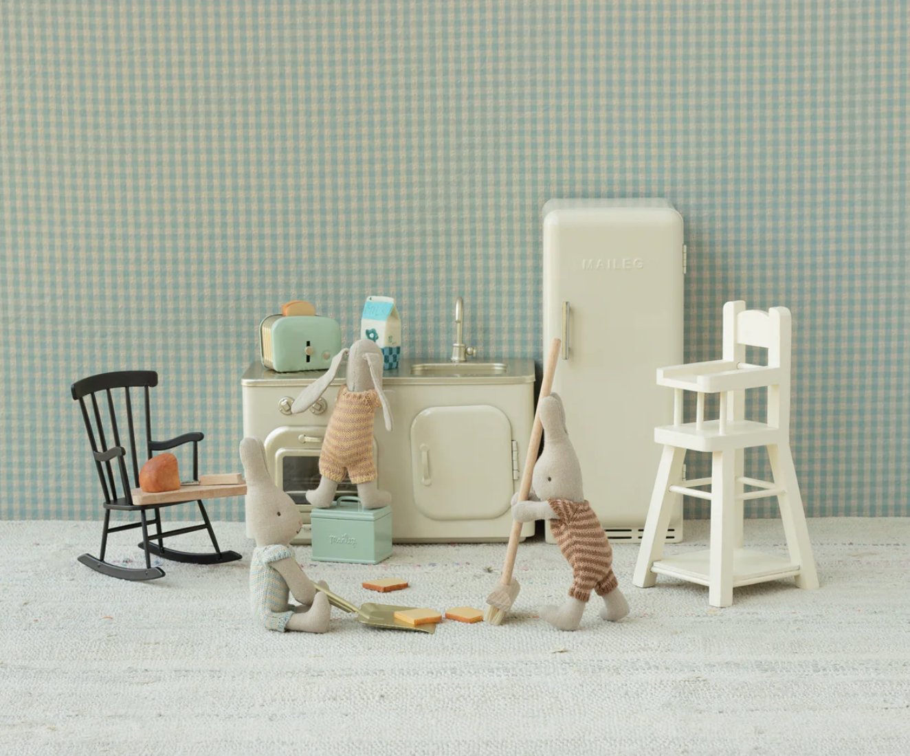 Miniature kitchen set with dollhouse furniture and accessories on a checkered floor.