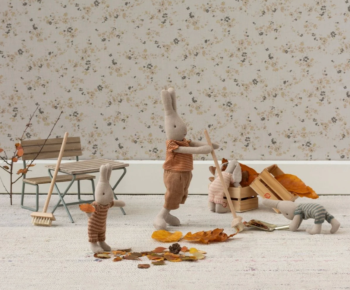 Toy rabbits in a playful arrangement with autumn leaves and a floral-patterned wall.