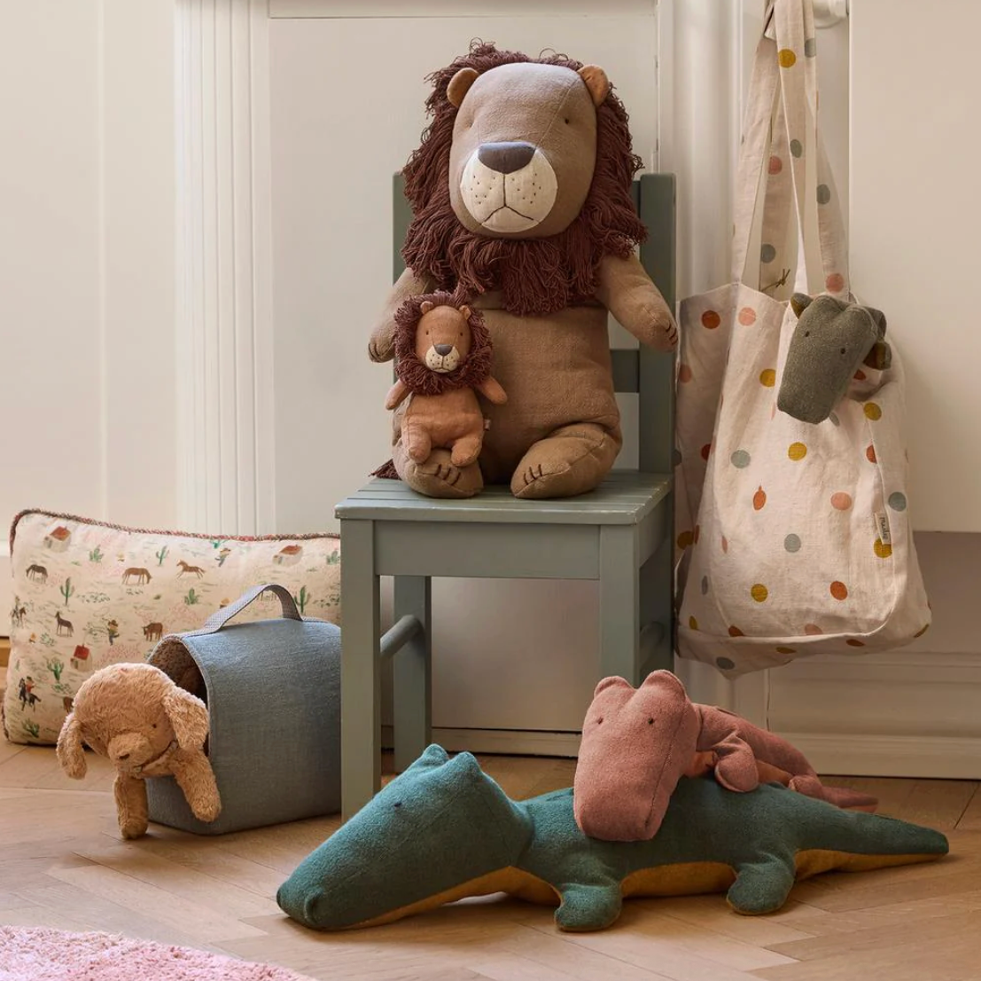 Plush toys including a lion, teddy bear, and dinosaur on a chair and floor.