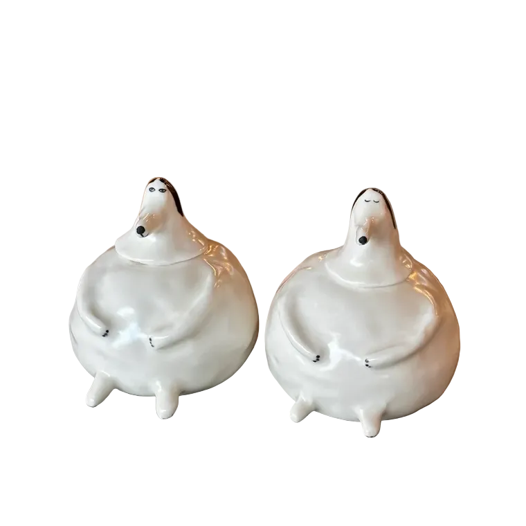 Two white ceramic jars on a stone surface with green chairs in the background.